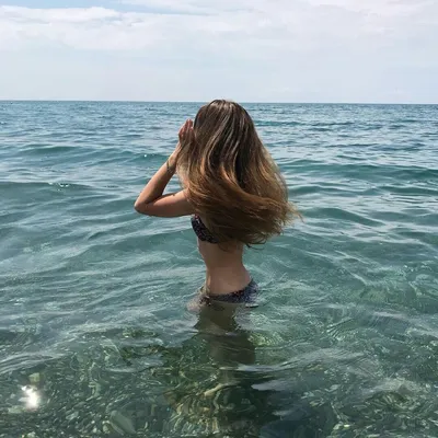 Девушка в шляпе и купальнике сидит на пляже спиной к камере и протягивает  руки вверх | Премиум Фото