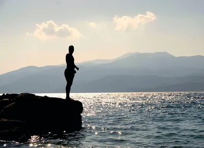 Человек, стоящий на скале возле моря возле острова в дневное время ·  Бесплатные стоковые фото